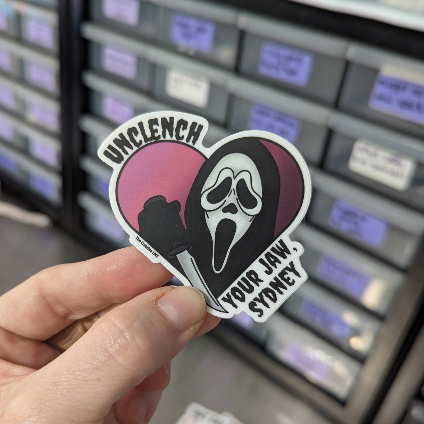 Hand holding a sticker with a graphic design in front of a storage unit.