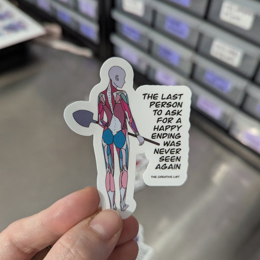 Hand holding a sticker with a character and text, against a blurred storage background.