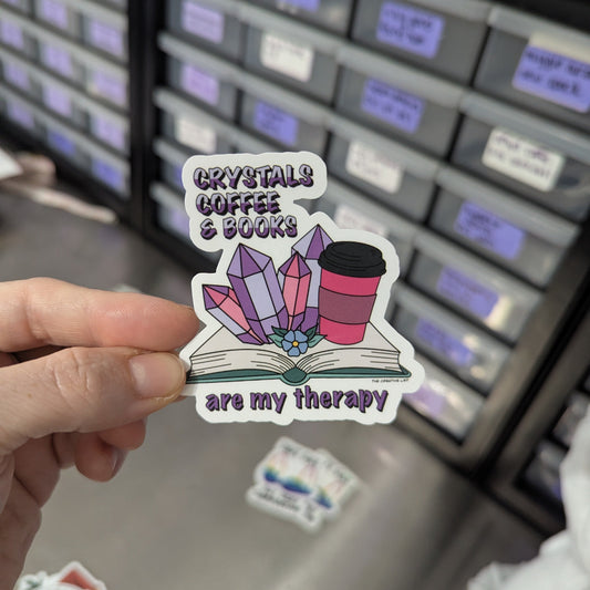 Sticker with crystals, coffee, and books design held in front of a storage unit.